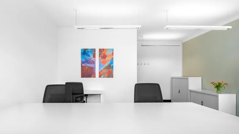 Heller Büroraum mit modernen Möbeln, Kunstwerken an der Wand und linearer Beleuchtung.