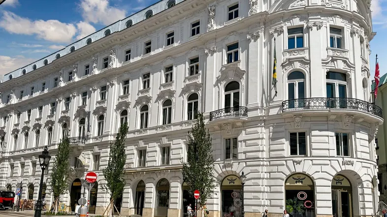 Eindrucksvolles, weißes Gebäude mit klassischer Architektur und vielen Fenstern an einer belebten Straße.