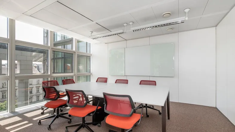 Moderner Konferenzraum mit großem Tisch, orangefarbenen Stühlen und viel Tageslicht durch große Fenster.