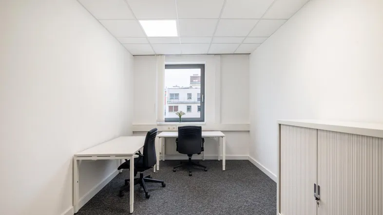 Helles Einzelbüro mit zwei Arbeitsplätzen, Fenster und Teppichboden in einem modernen Gebäude.