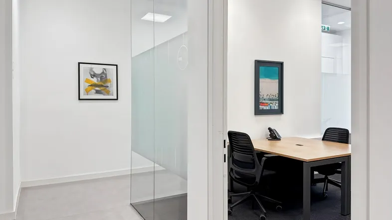 Moderner Bürobereich mit Glaswänden und einem privaten Arbeitsplatz, ausgestattet mit Schreibtisch und Stühlen.