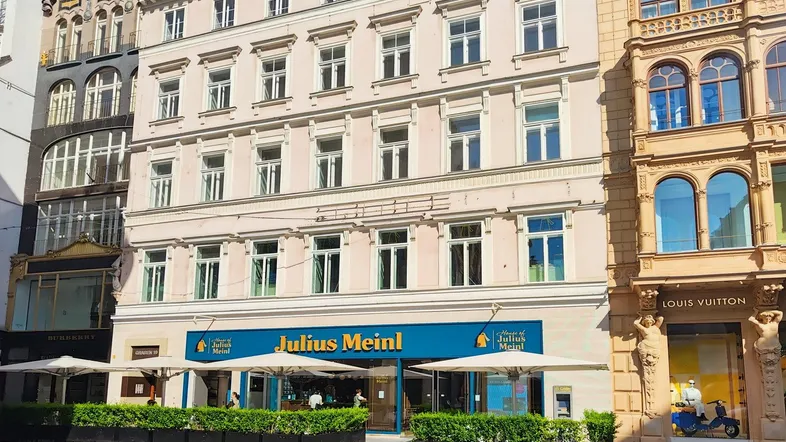 Historisches Gebäude mit klassischer Fassade und Geschäften im Erdgeschoss an einer belebten Straße.