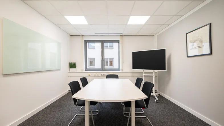 Moderner Konferenzraum mit großem Tisch, Whiteboard und Bildschirm für Präsentationen.