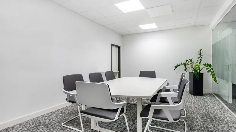 Moderner Konferenzraum mit weißem Tisch, grauen Stühlen und Teppichboden, ideal für Besprechungen.