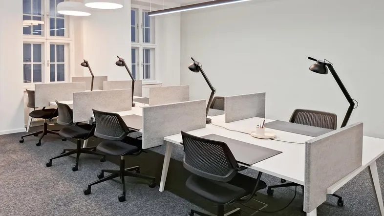 Moderne Büroräume mit mehreren Arbeitsplätzen, ergonomischen Stühlen und großen Fenstern für natürliches Licht.