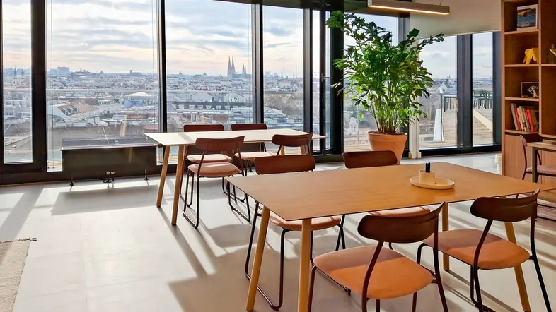 Heller Gemeinschaftsbereich mit großen Fenstern, die einen weiten Blick über die Stadt bieten und viel Tageslicht hereinlassen.