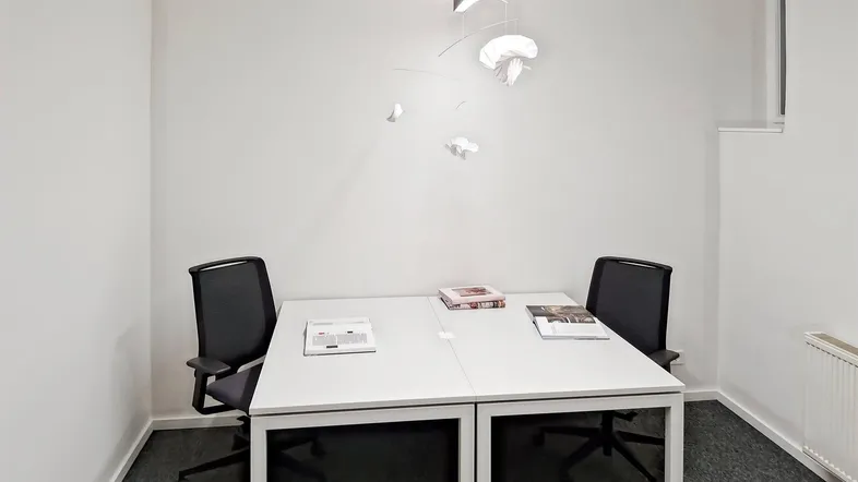 Modernes Büro mit zwei Arbeitsplätzen, weiß gestrichenen Wänden und grauem Teppichboden.