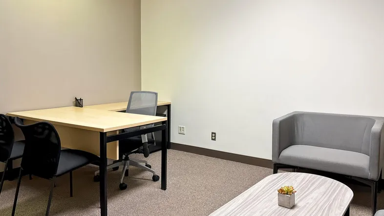 Helles Büro mit Schreibtisch, Bürostuhl und kleiner Sitzecke, ideal für konzentriertes Arbeiten oder Besprechungen.