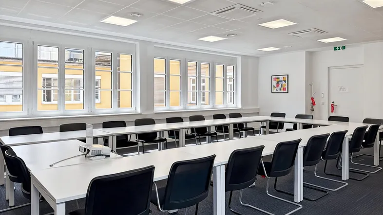 Großer Konferenzraum mit U-förmigem Tisch, vielen Fenstern und einem Beamer für professionelle Präsentationen.