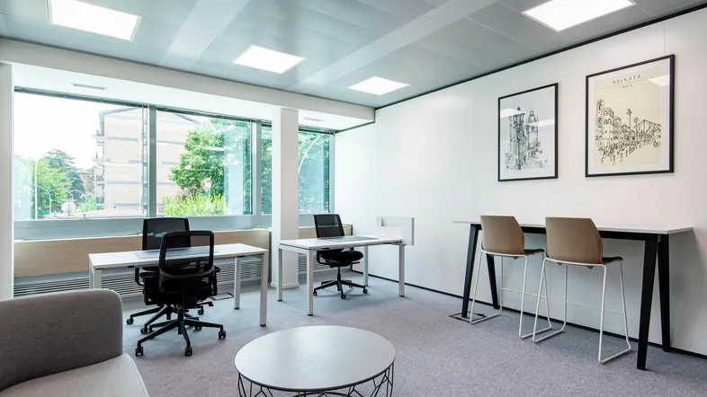 Modernes Büro mit großen Fenstern, mehreren Arbeitsplätzen und einer kleinen Lounge-Ecke für Besprechungen.