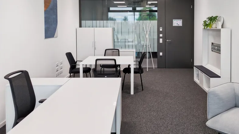 Modernes Büro mit mehreren Arbeitsplätzen, einem Besprechungstisch und einem Eingangsbereich mit Garderobe.