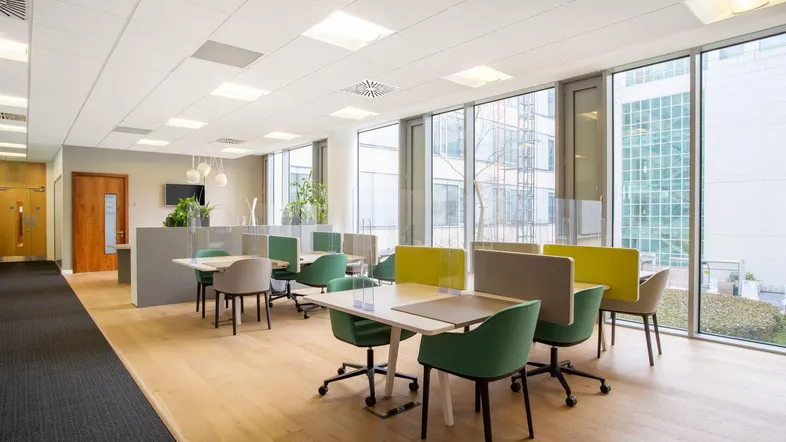 Moderner Großraumbüro-Bereich mit hellen Holzfußböden, großen Fenstern und ergonomischen Sitzgelegenheiten für konzentriertes Arbeiten.