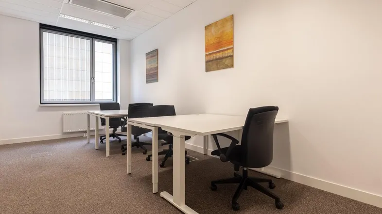 Modernes Büro mit mehreren Arbeitsplätzen, Teppichboden und großen Fenstern für natürliches Licht.