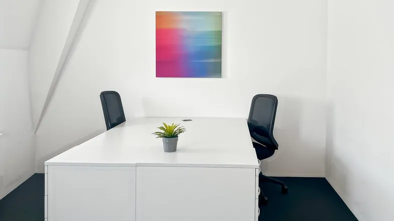 Modernes Büro mit weißem Schreibtisch, zwei Stühlen und farbenfrohem Kunstwerk an der Wand.