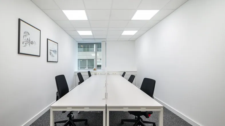 Moderner Büroraum mit langen Schreibtischen, ergonomischen Stühlen und Teppichboden, ideal für Teamarbeit.