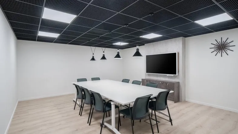 Moderner Konferenzraum mit großem Tisch, Multimedia-Bildschirm und einer auffälligen schwarzen Gitterdecke.
