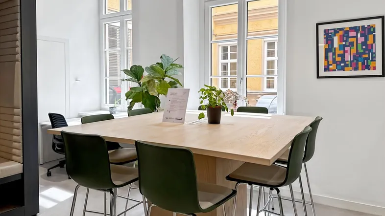 Moderner Besprechungsraum mit großem Holztisch, hohen Fenstern und grünen Stühlen.