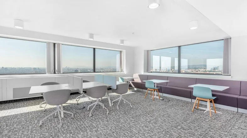Moderner Büroraum mit flexiblen Arbeitsplätzen, bequemen Sitzgelegenheiten und weitem Stadtblick durch große Fenster.