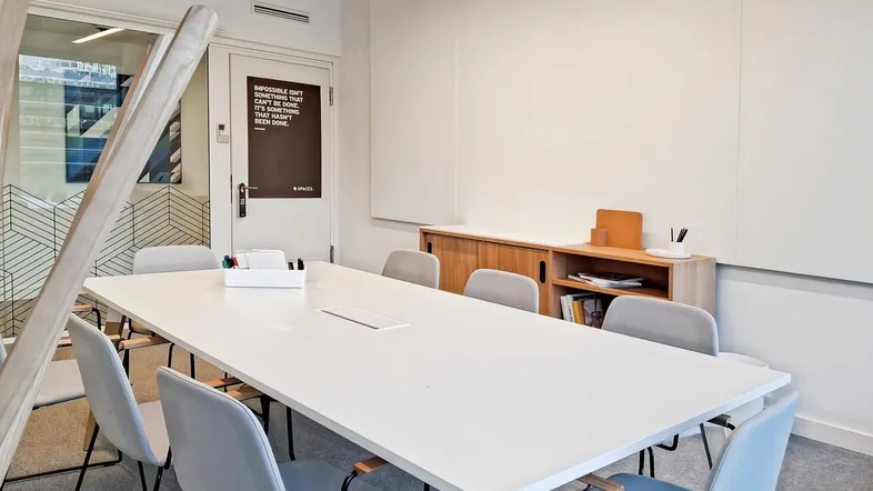 Moderner Konferenzraum mit großem weißen Tisch, bequemen Stühlen und einer Whiteboard-Wand für Präsentationen.