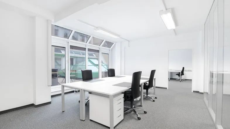 Helles und modernes Büro mit mehreren Arbeitsplätzen, großen Fenstern und Blick auf einen Innenhof.