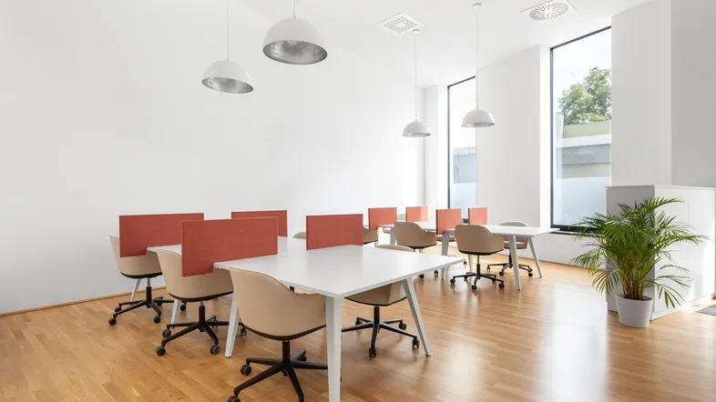 Heller, moderner Büroraum mit mehreren Arbeitsplätzen, großen Fenstern und Holzfußboden.