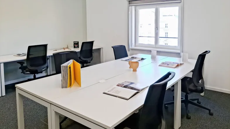 Modernes Büro mit mehreren Arbeitsplätzen, großen Fenstern und Teppichboden für eine produktive Umgebung.