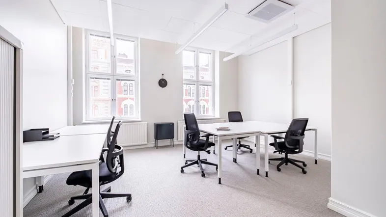 Helles und geräumiges Büro mit mehreren Arbeitsplätzen, großen Fenstern und Teppichboden für eine angenehme Arbeitsatmosphäre.