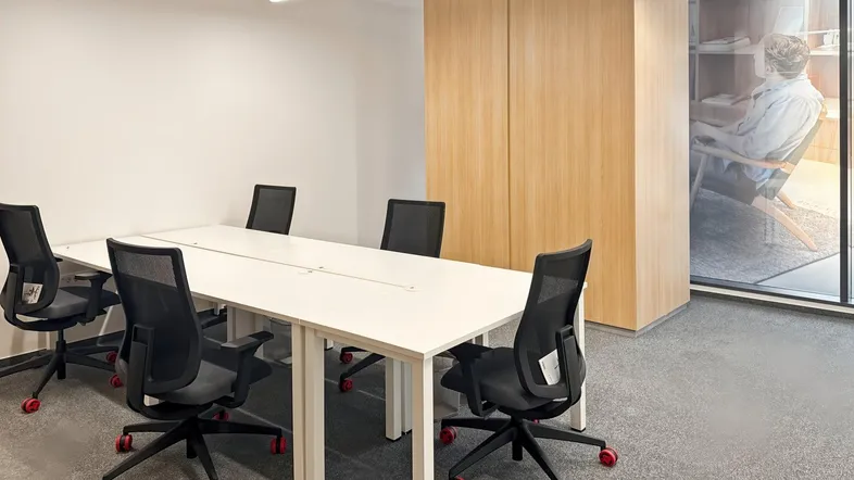 Moderner Büroraum mit einem langen weißen Konferenztisch, ergonomischen Stühlen und hellen Holzschränken.