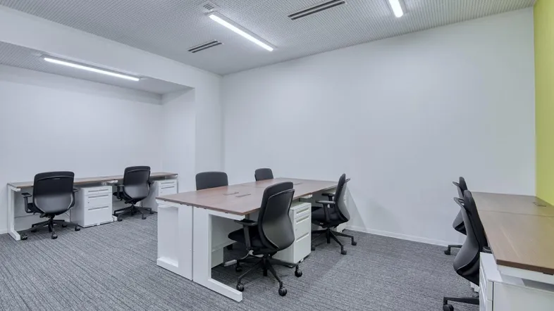 Geräumiges, modernes Büro mit mehreren Schreibtischen, ergonomischen Stühlen und Teppichboden.
