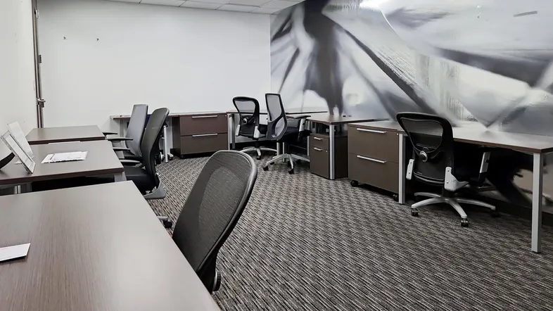 Großraumbüro mit mehreren Schreibtischen, ergonomischen Stühlen und einem modernen Wandbild an der Akzentwand.