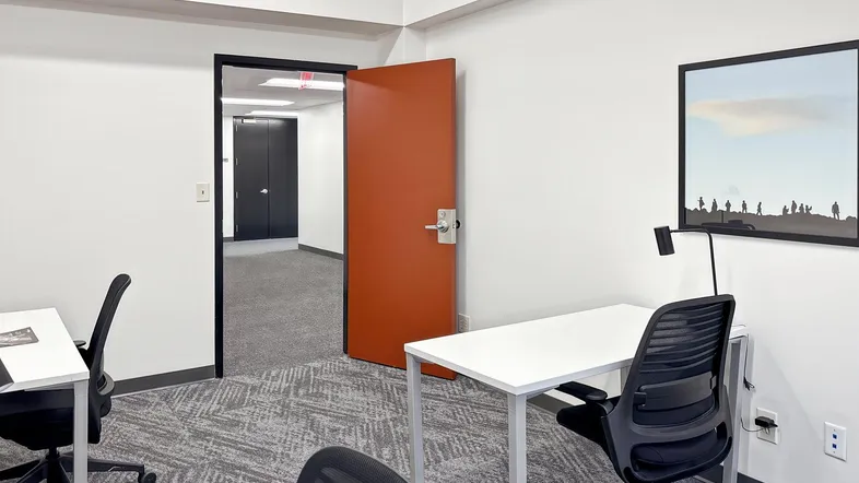 Modernes Büro mit zwei Arbeitsplätzen, grauem Teppichboden und einer auffälligen orangefarbenen Tür.
