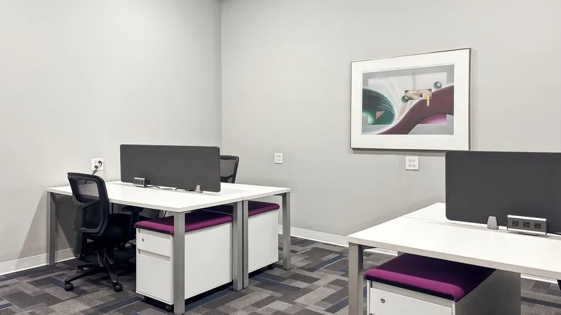 Modernes Büro mit zwei Arbeitsplätzen, Teppichboden und einem gerahmten Bild an der hellgrauen Wand.