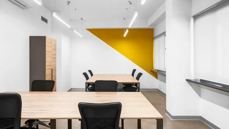 Modernes Büro mit mehreren Arbeitsplätzen, einer gelben Akzentwand und Betonboden.