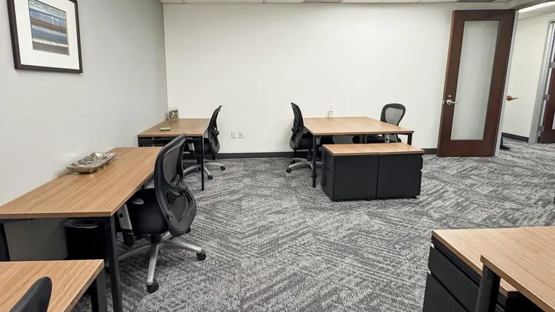 Großraumbüro mit mehreren Schreibtischen, Bürostühlen und Teppichboden in modernem Design.