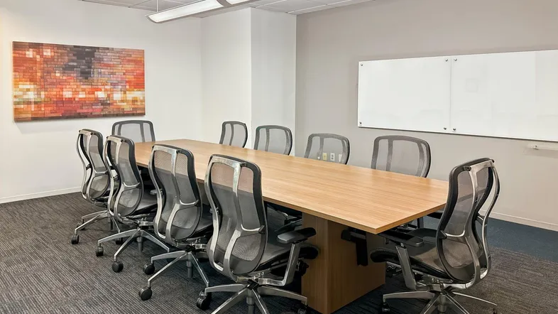 Geräumiger Konferenzraum mit großem Holztisch, ergonomischen Stühlen und einer Whiteboard-Wand für Besprechungen.