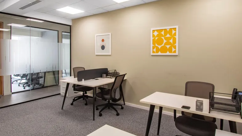 Modernes Büro mit mehreren Arbeitsplätzen, Glaswänden und beigen Wänden, ideal für Teamarbeit.