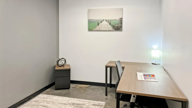 Modernes Einzelbüro mit Schreibtisch, Teppich und Wandkunst in neutralen Farben für eine angenehme Arbeitsatmosphäre.