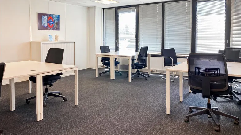 Modernes Büro mit mehreren Arbeitsplätzen, Teppichboden und großen Fenstern mit Jalousien.