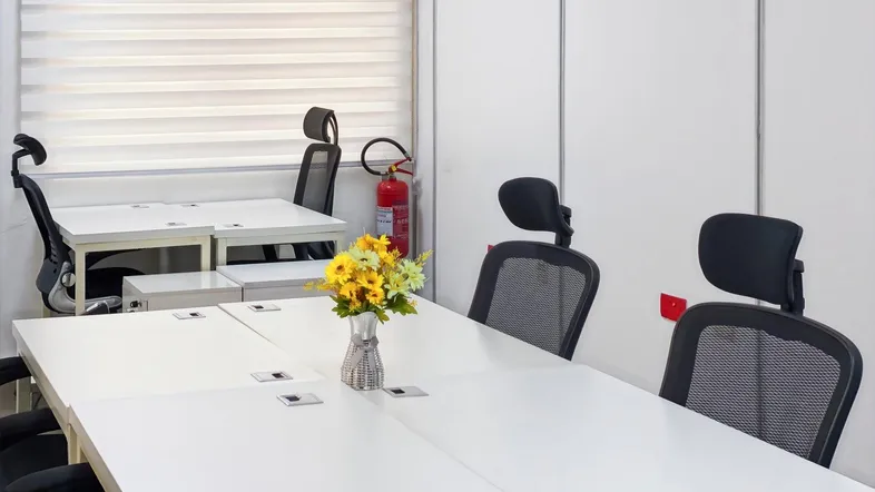 Heller Büroraum mit mehreren Arbeitsplätzen, weißen Tischen und ergonomischen Stühlen.