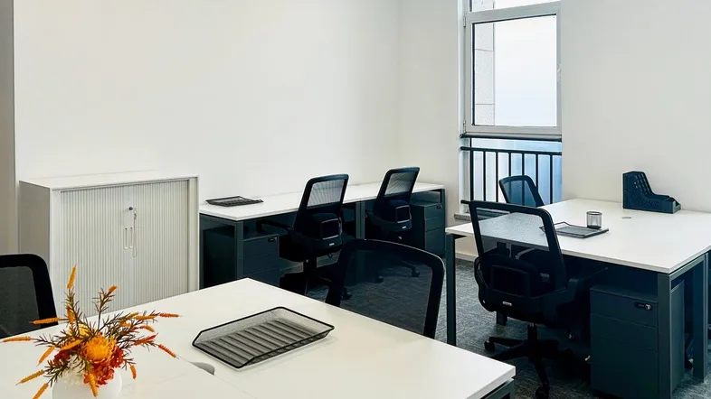 Modernes Büro mit mehreren Arbeitsplätzen, weißen Schreibtischen und einem Fenster für natürliches Licht.