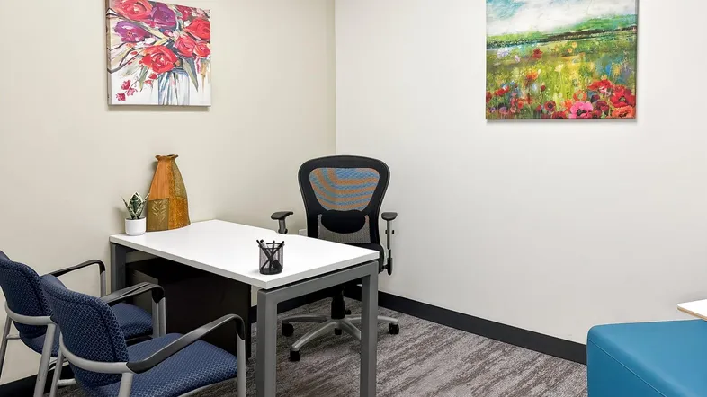 Kleines, helles Büro mit Schreibtisch, Bürostuhl und zwei Bildern an den Wänden, ideal für konzentriertes Arbeiten.
