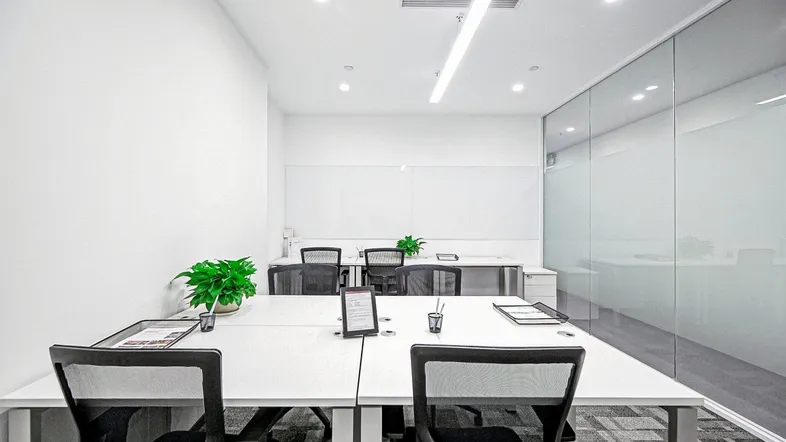 Moderner Büroraum mit weißen Schreibtischen, ergonomischen Stühlen und einer Glaswand für offene Arbeitsbereiche.