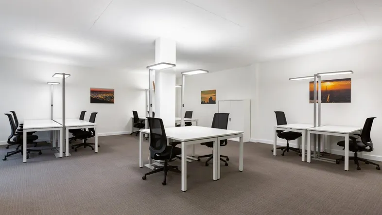 Heller Großraumbüro mit mehreren Arbeitsplätzen, Teppichboden und modernen Büromöbeln.