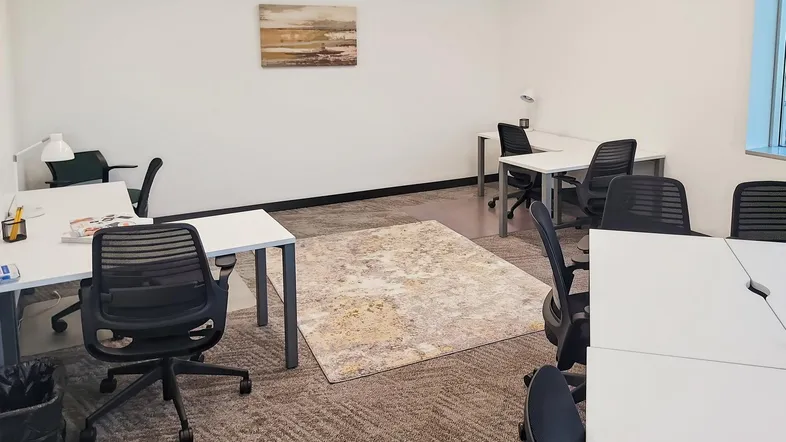 Geräumiges Büro mit mehreren Arbeitsplätzen, Teppichboden und einem dekorativen Teppich in der Mitte.