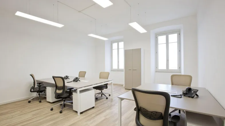 Helles und geräumiges Büro mit mehreren Arbeitsplätzen, großen Fenstern und Holzfußboden.