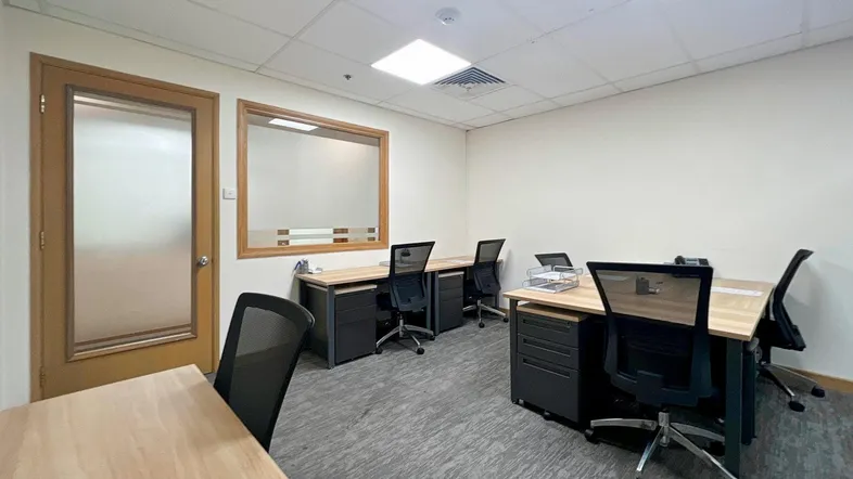 Modernes Büro mit mehreren Arbeitsplätzen, Teppichboden und einer Glaswand zu einem weiteren Raum.