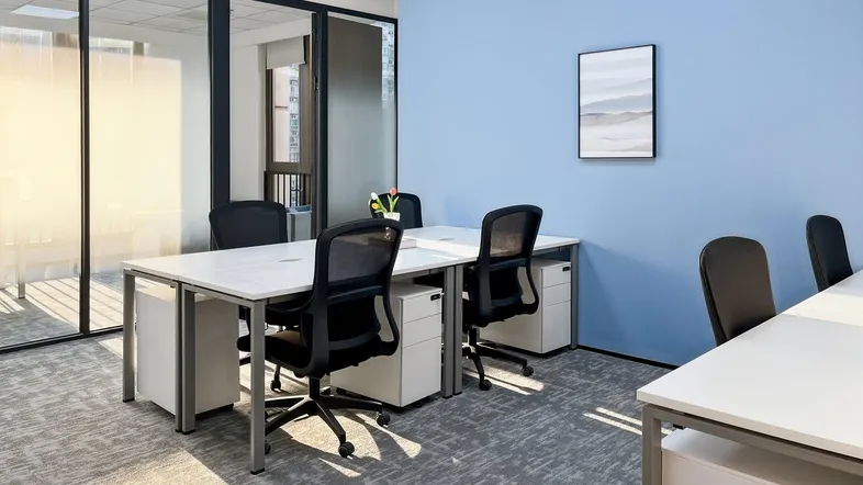 Modernes Büro mit hellblauen Wänden, Teppichboden und Arbeitsplätzen mit Blick nach draußen.