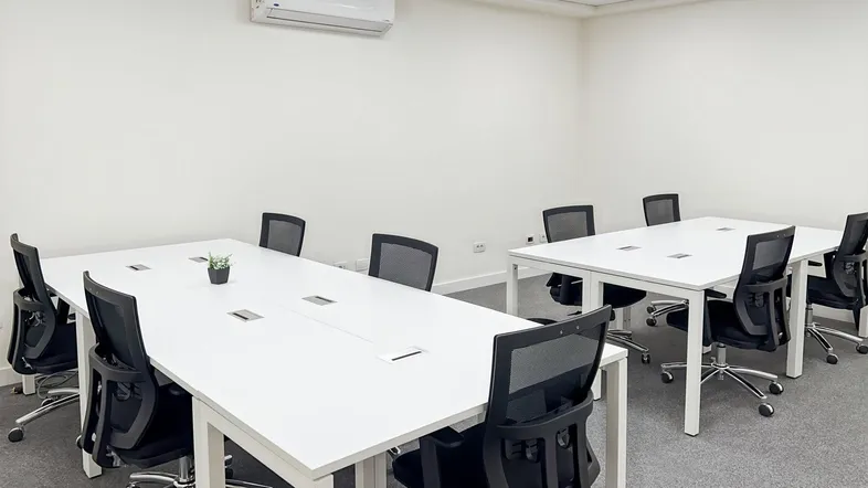 Heller Konferenzraum mit mehreren weißen Tischen und ergonomischen Stühlen, ideal für Besprechungen und Teamarbeit.