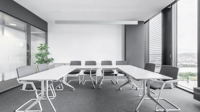 Moderner Konferenzraum mit flexiblen Tischen, Teppichboden und großen Fenstern mit Stadtblick.