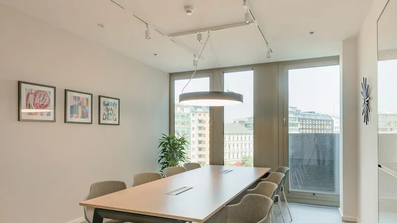 Moderner Konferenzraum mit großem Holztisch, bequemen Stühlen und viel Tageslicht durch bodentiefe Fenster.